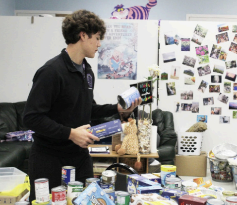 FOR THE NEEDY: Junior Jesse Profeta grabs food items while working to assemble Thanksgiving baskets in Ms. Russell's office. 